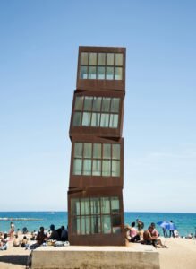 Cubic metal blocks placed on top of each other on concrete stand on sandy beach full of people